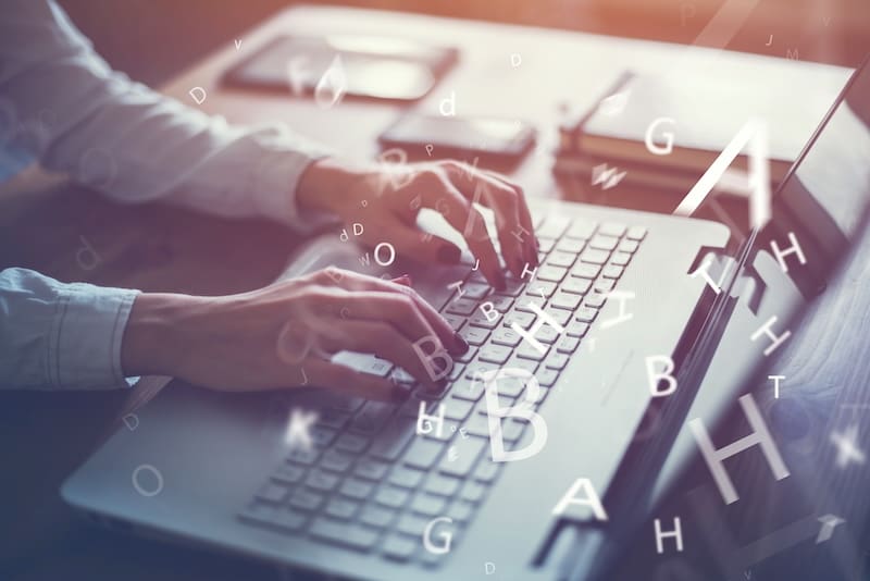 Hands typing on a laptop keyboard with large, floating letters and symbols superimposed over the image. A soft light filters through the scene, inspiring you to start a blog in this focused and creative atmosphere.