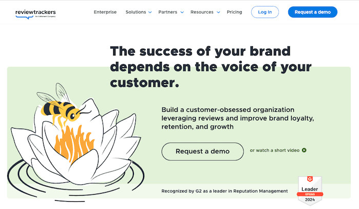 An online platform's webpage features a large text saying, "The success of your brand depends on the voice of your customer." A bee sits on a white flower illustration. There are buttons for "Request a demo" and watching a short video. The page highlights its reputation as the best review management software with a G2 leader badge for Spring 2024.