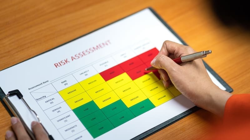 A person holds a pen and marks a red section on a risk assessment chart, key to corporate reputation management, placed on a clipboard. The chart is color-coded into green, yellow, and red sections, indicating different levels of risk severity. The clipboard rests on a wooden surface.
