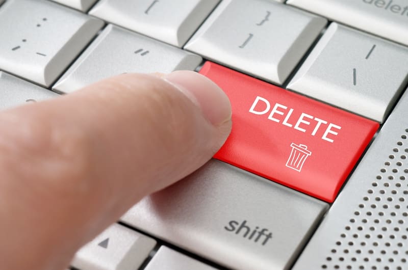 A close-up of a finger pressing a large red keyboard key labeled "DELETE," adorned with a trash can icon. The surrounding silver keys glint, hinting at the "Shift" key nearby—reminding one of Georgia's new mugshot law about erasing the past with just a touch.