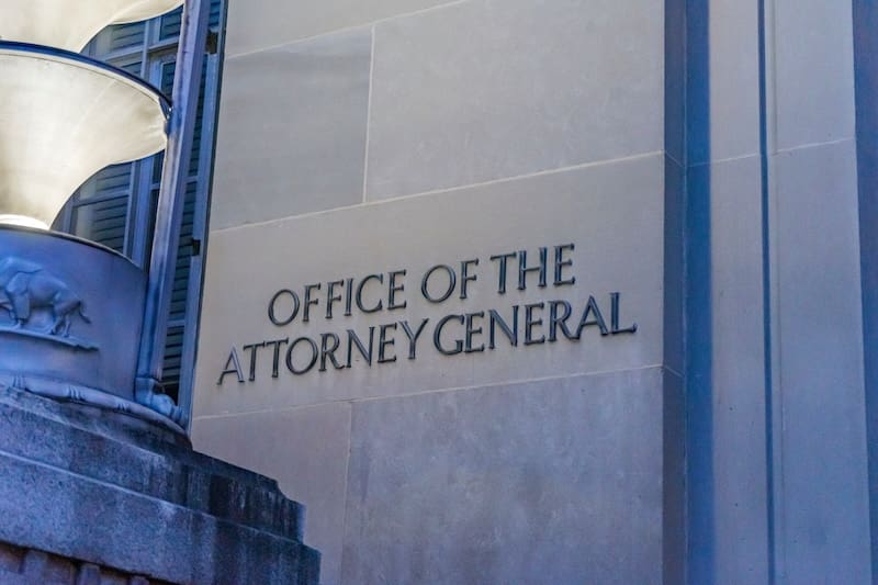 The image shows a stone building wall with the engraved text "Office of the Attorney General." A decorative stone structure with a relief motif is partially visible on the left, symbolizing Georgia's commitment to upholding its mugshot law.