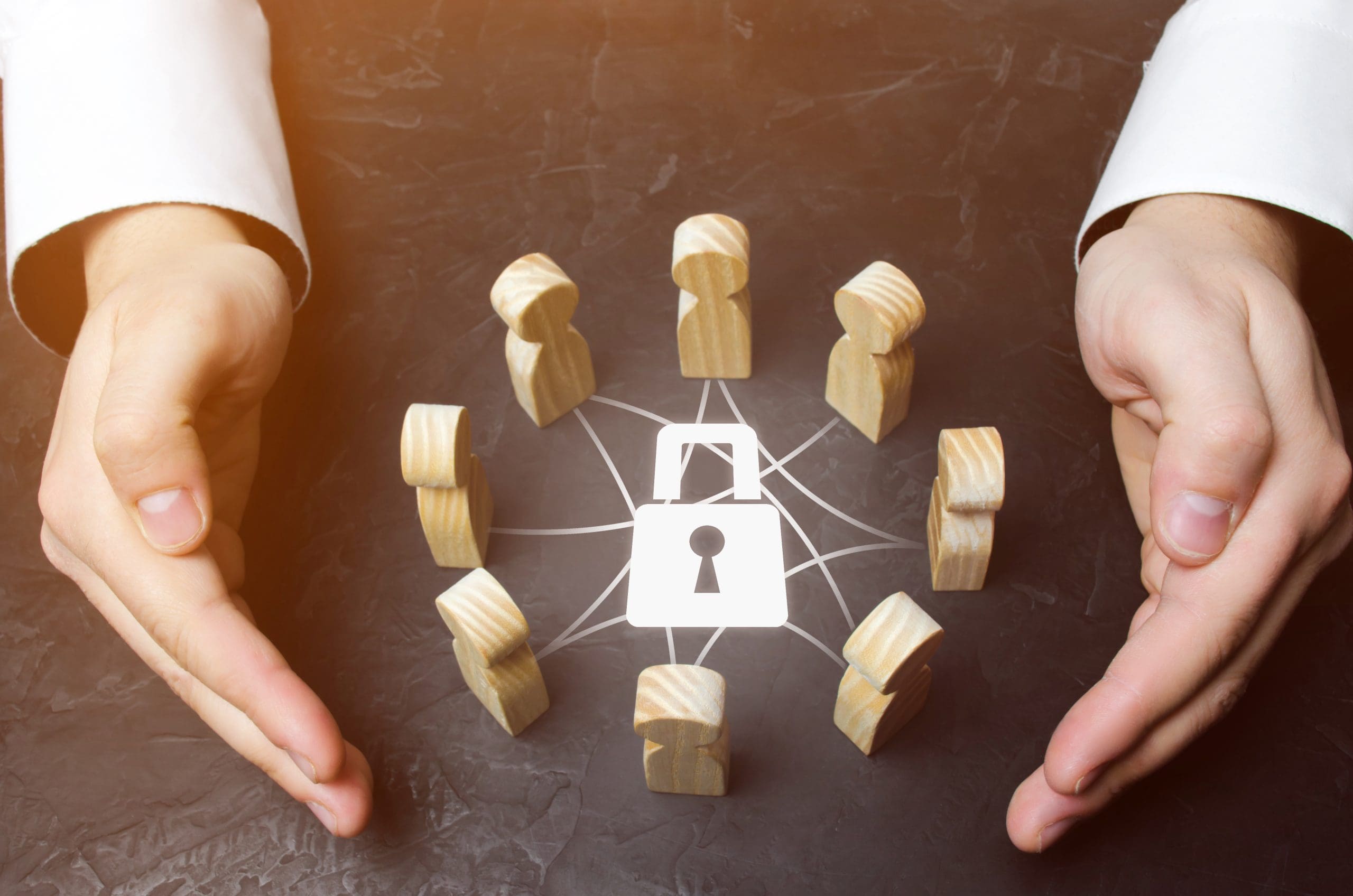 Hands encircle a group of wooden figures connected by lines, with a padlock symbol in the center. The setup suggests themes of security, protection, or network safety.