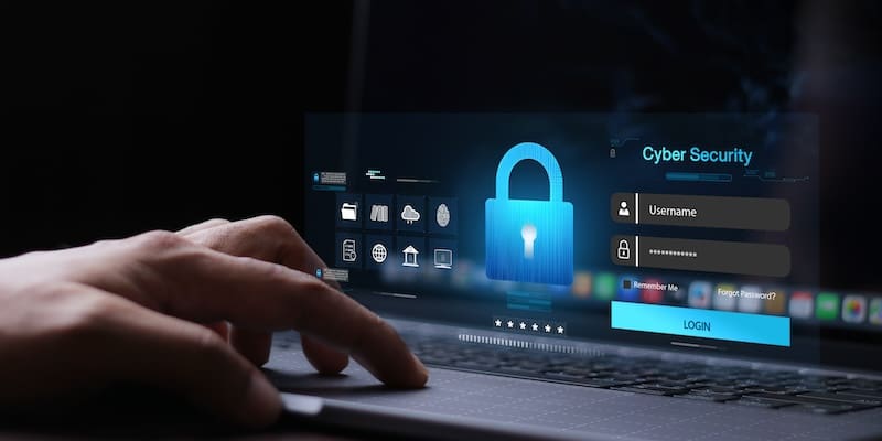 A hand typing on a laptop, with a holographic display showing a lock icon, login interface, and the words "Cyber Security." Various digital icons are visible in the background, symbolizing secure data and online protection.