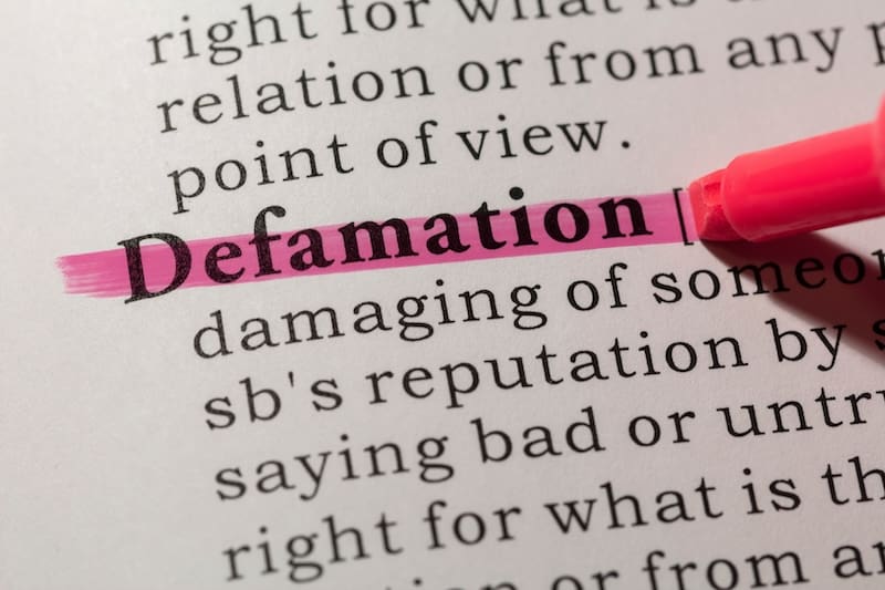 The word "Defamation" is highlighted in pink on a page, hinting at the need for an online content removal lawyer. A pink highlighter peeks from the right, while the surrounding text remains slightly blurred yet readable.