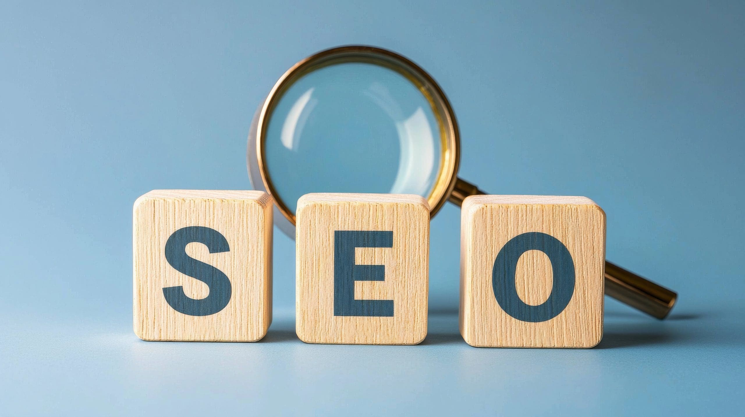 Wooden blocks spelling "SEO" sit in front of a magnifying glass, symbolizing the clarity expert SEO services bring to your digital strategy, all set against a blue background.