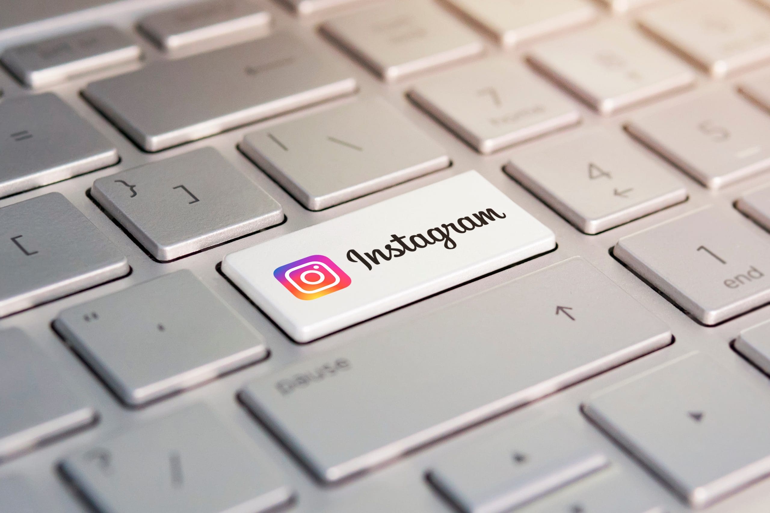 A close-up of a computer keyboard with the "Enter" key replaced by a white key featuring the Instagram logo and text. The surrounding keys are grey, and soft light highlights the keyboard.