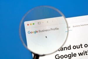 A magnifying glass focusing on the "Google Business Profile" webpage on a computer screen. The website's header is visible, displaying colorful text on a clean, white background.