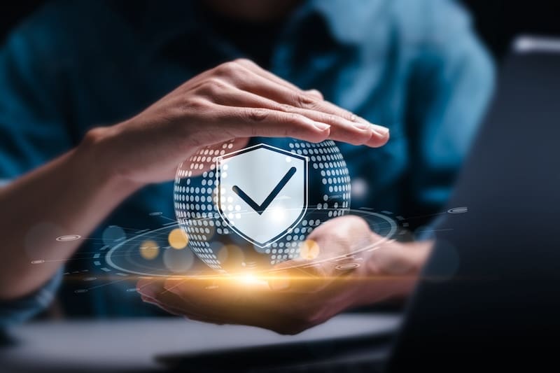 A person holds a glowing digital globe with a shield and checkmark symbol, symbolizing the CEO's commitment to cybersecurity and information privacy, in front of a blurred background.