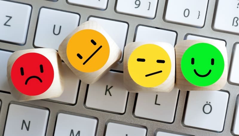 Wooden blocks with colorful emoticons—red sad face, orange neutral face, yellow indifferent face, and green happy face—placed on a computer keyboard symbolize how to deal with bad reviews.